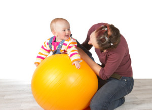 Devoted mother exercising her laughing baby who has late development of motor activity using a yellow pilates ball